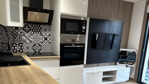 A modern kitchen with a built-in oven, microwave, and a large TV mounted on the wall.
