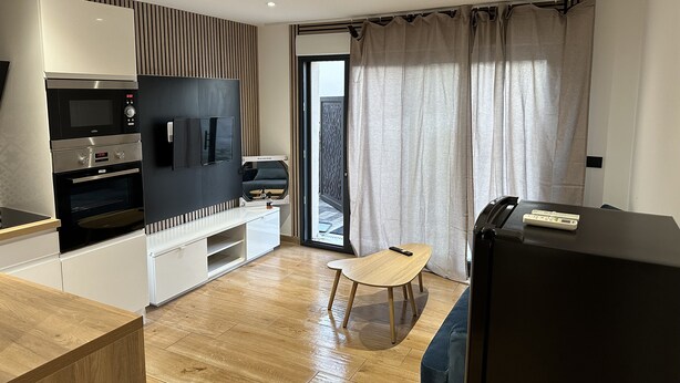 A modern kitchen with built-in appliances, a dining area with a wooden table and chair, and a large window with curtains.