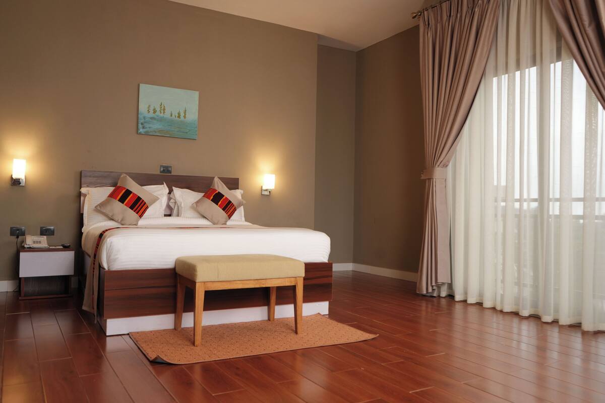 A neatly arranged bedroom with a large bed, bedside lamps, a nightstand, and a painting on the wall.
