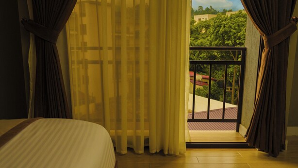 Ein Hotelzimmer mit Bett, Vorhängen und einem Balkon mit Blick auf Grünflächen.