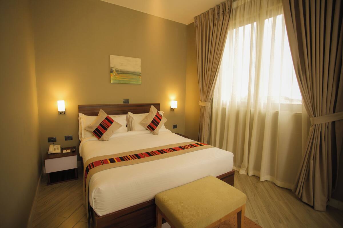 A neatly made bed with a striped blanket, bedside lamps, and a painting on the wall.