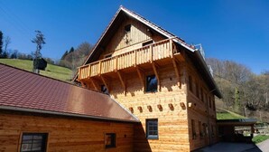 Een houten chalet met schuin dak, een balkon en uitzicht op het omliggende landschap.