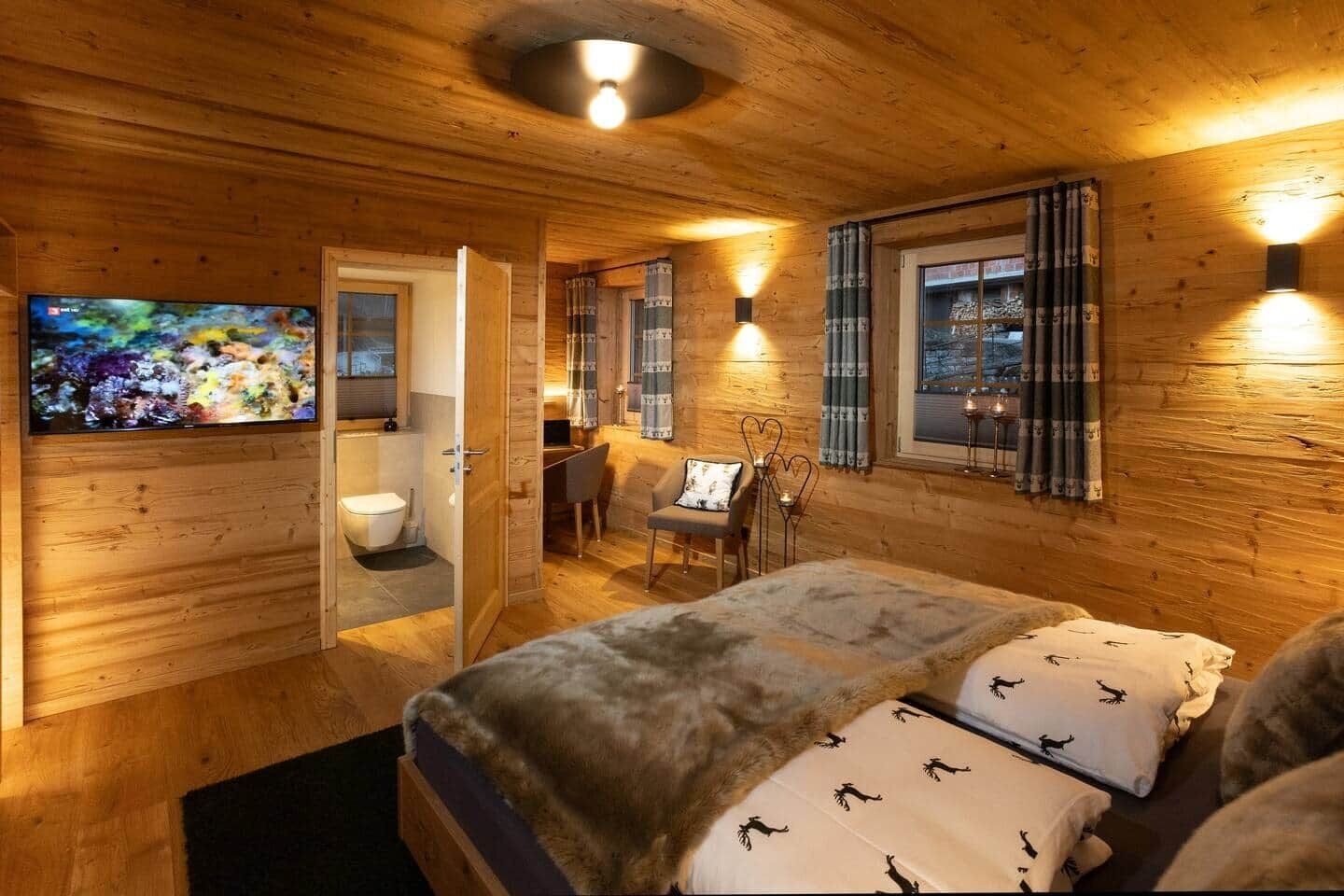 Ein gemütliches Holzhütten-Zimmer mit Bett, Schreibtisch, Stuhl, Fernseher und Bad.