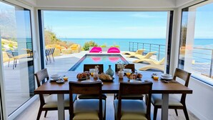 A dining area with a view of the sea, a pool, and outdoor seating. - Aux 3 Bains - Plage, Piscine, Spa (Locquirec)