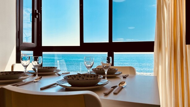 A dining table set with plates, bowls, and cutlery, overlooking a coastal view through large windows. - Bright Sun House with Sea Views (Agüimes)