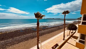 A beach view with a rocky shoreline, palm trees, and a building with a tiled walkway. - Bright Sun House with Sea Views (Agüimes)