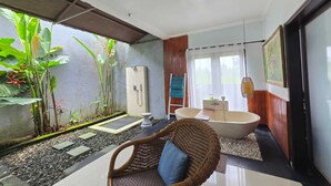 A bathroom with a bathtub, a shower, and a sink. There are plants and a wicker chair. - Belvilla Kasuari Tirta Empul Temple (Taro)