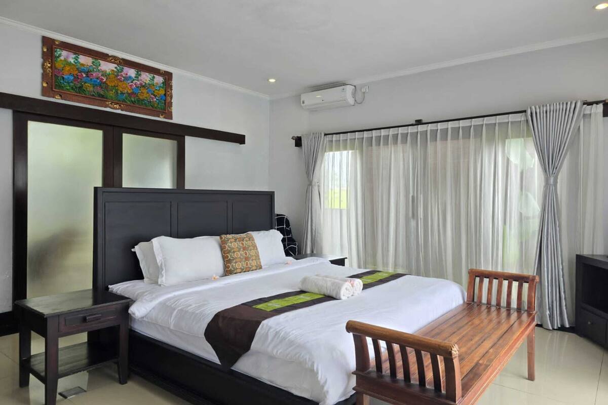 A hotel room with a large bed, a wooden bench, a desk, and a TV.