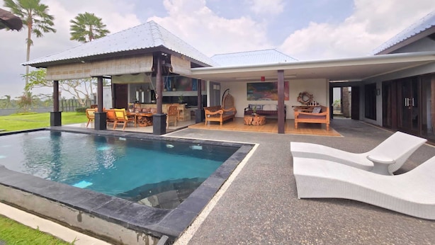 A poolside area with a lounge chair, a covered patio, and a dining setup. - Belvilla Kasuari Tirta Empul Temple (Taro)