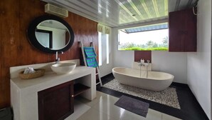 A modern bathroom with a freestanding bathtub, a round mirror, and a wooden vanity. - Belvilla Kasuari Tirta Empul Temple (Taro)