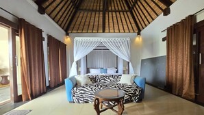 A room with a zebra-patterned sofa, a round wooden table, and a canopy bed. - Belvilla Kasuari Tirta Empul Temple (Taro)