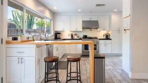 A modern kitchen with white cabinets, a wooden island, two stools, and a stainless steel refrigerator. - Yorba Linda Furnished Retreat with Pool and Spa (Yorba Linda)