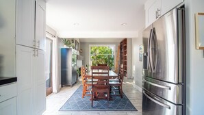 A modern kitchen with white cabinetry, a stainless steel refrigerator, and a dining area with a wooden table and chairs. - Yorba Linda Furnished Retreat with Pool and Spa (Yorba Linda)