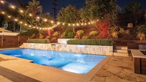 A swimming pool with a waterfall feature, surrounded by a landscaped garden with various plants and trees. - Yorba Linda Furnished Retreat with Pool and Spa (Yorba Linda)