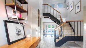 A spacious hallway with a wooden desk, a staircase with black railings, and framed artwork on the walls. - Yorba Linda Furnished Retreat with Pool and Spa (Yorba Linda)
