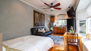 Een slaapkamer met een bed, een plafondventilator, een eettafel met een stoel en een keuken op de achtergrond.