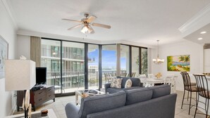 Un salon moderne avec un canapé gris, un téléviseur et un coin repas comprenant une table et des chaises.