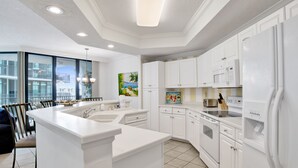 Une cuisine moderne avec des meubles blancs, un îlot central et un coin repas offrant une vue sur la ville.