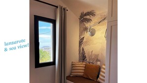 Ein Zimmer mit Fenster und Meerblick, einer Wandmalerei und einer Sitzbank mit Kissen.
