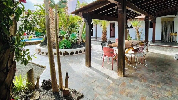 Ein Patio mit Holz-Pergola, Steinboden und einem Esstisch mit Stühlen.