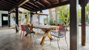 Un pati exterior amb taula i cadires de fusta, envoltat de plantes en testos i una pèrgola de fusta.