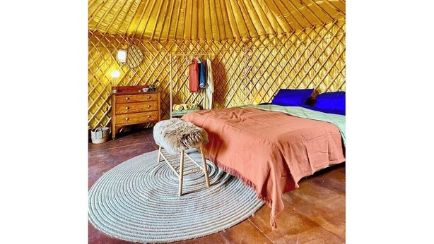 Una habitació amb un sostre circular, un llit amb edredó rosa, un taulell de fusta, una catifa rodona i una làmpada penjant.
