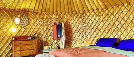 Ein Zimmer mit kreisrunder Decke, einem Bett mit rosa Bettdecke, einem hölzernen Schminktisch, einem runden Teppich und einer Pendelleuchte.