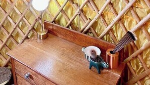 Habitació amb paret de bambú, tocador de fusta amb mirall i taula petita amb una làmpada i un objecte decoratiu.