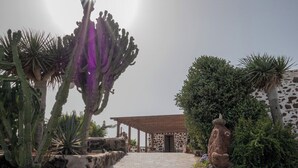A pathway leading to a building with a stone facade and a wooden roof. - Co-Living at Casa Cocolores (La Oliva)