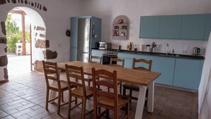 A kitchen with a wooden table and chairs, a blue cabinet, a refrigerator, and a stove. - Co-Living at Casa Cocolores (La Oliva)