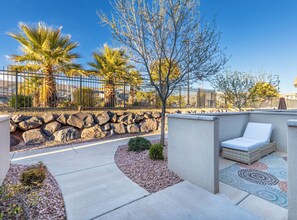 A patio area with a stone wall, a small tree, and a lounge chair.