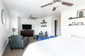 A hotel room with a bed, a TV, a desk, a chair, a ceiling fan, and a door. - The Vintage- Poolside 3 bed 2.5 bath (Washington)