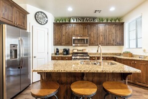 A kitchen with wooden cabinets, stainless steel appliances, a granite countertop, and a bar stool seating area.