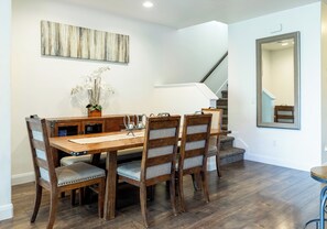 Un coin repas avec une table et des chaises en bois, un vase rempli de fleurs et un escalier en arrière-plan.