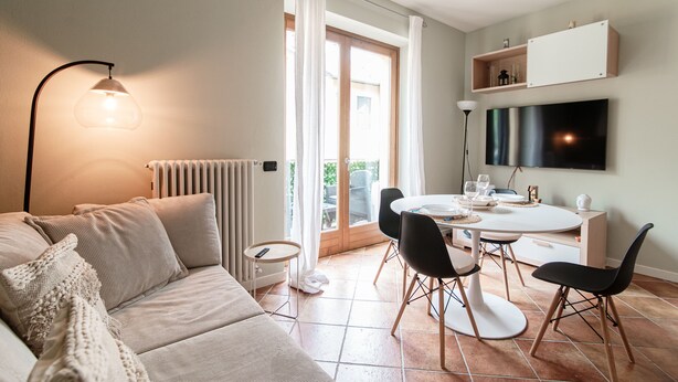 Una sala de estar moderna con sofá, una mesa de comedor con sillas, televisor montado en la pared y puerta corrediza de vidrio que da a un área exterior.