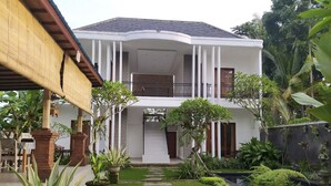 Ein zweigeschossiges Haus mit überdachter Terrasse, Kiesweg und üppiger Bepflanzung.