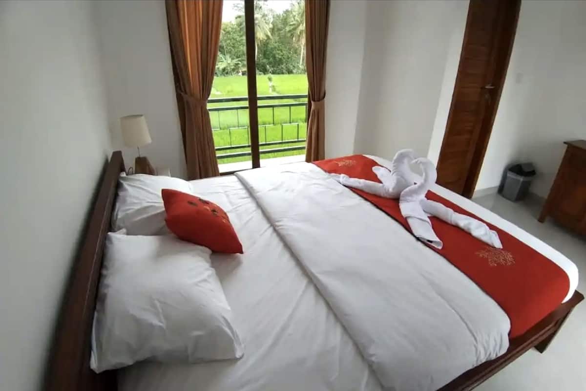 Ein Hotelzimmer mit einem Bett, weißer Bettwäsche, einem roten Kissen, einem Handtuch und Blick auf eine grüne Landschaft durch das Fenster.