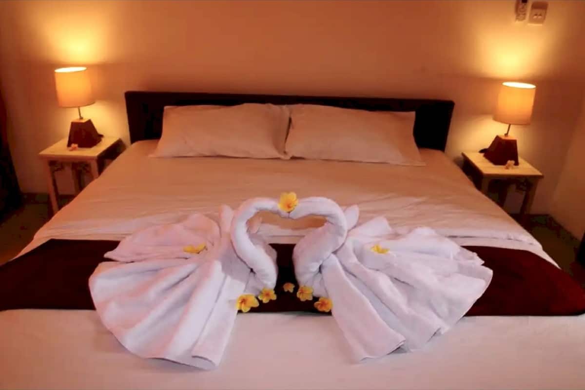 Ein ordentlich bezogenes Bett mit Handtüchern, die zu einem Herzen geformt sind, und zwei Nachttischlampen an jeder Seite.