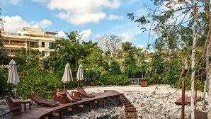 A wooden deck with lounge chairs and umbrellas overlooking a natural pool surrounded by greenery and a rocky landscape. - Splendid Penthouse, Rooftop Plunge Pool, 2 Cenotes (Tulum)