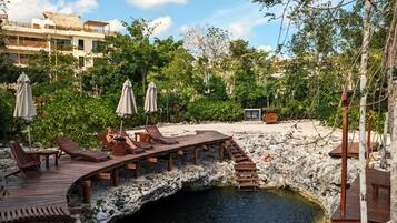 A wooden deck with lounge chairs and umbrellas overlooking a natural pool surrounded by greenery and a rocky landscape.