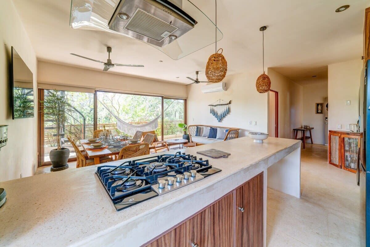 A modern kitchen with a central island, large windows, and a hammock outside.