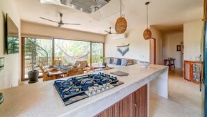 A modern kitchen with a central island, large windows, and a hammock outside. - Splendid Penthouse, Rooftop Plunge Pool, 2 Cenotes (Tulum)
