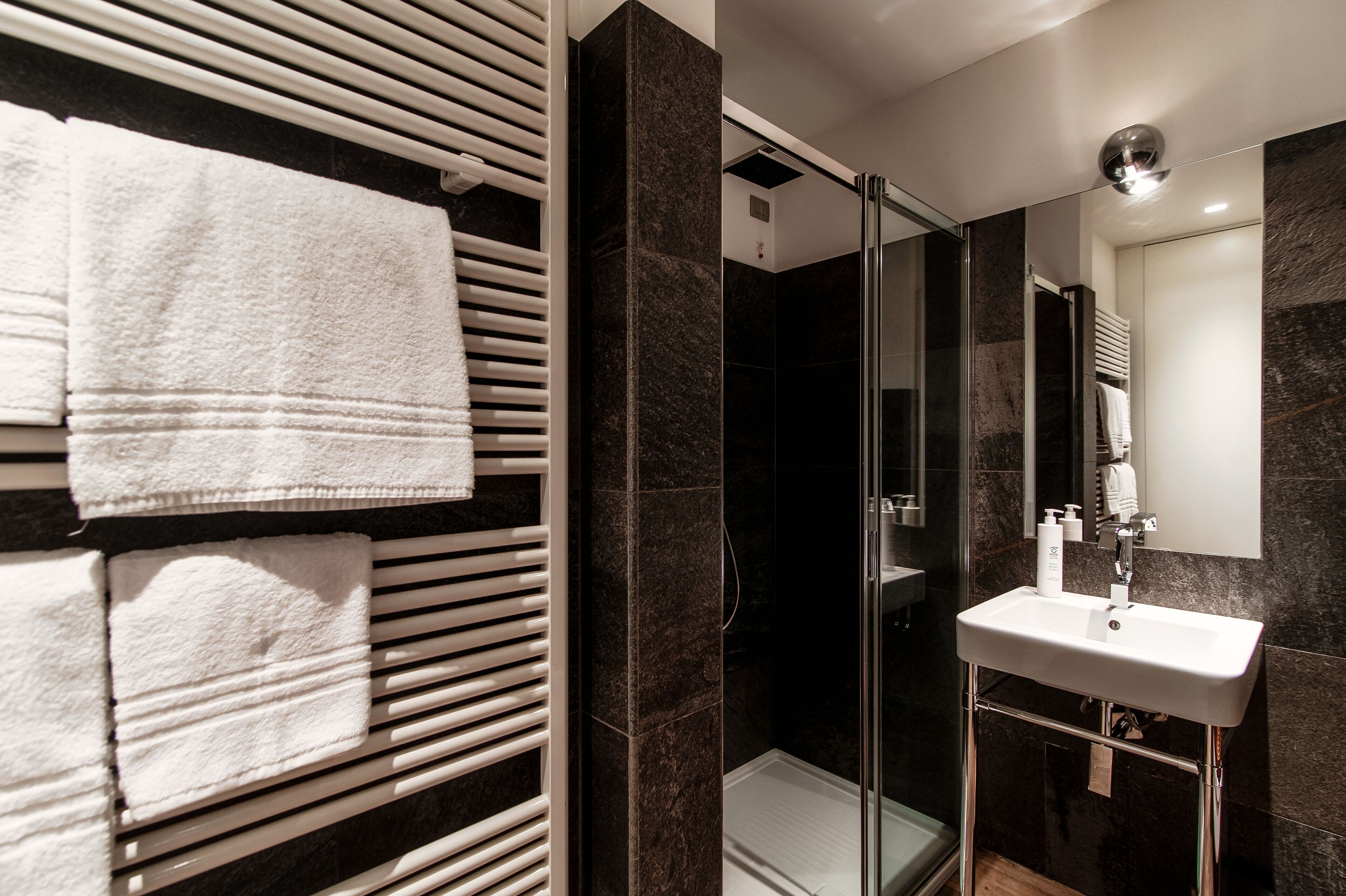 A modern bathroom with a glass shower enclosure, a white sink, and a towel rack with neatly folded towels.