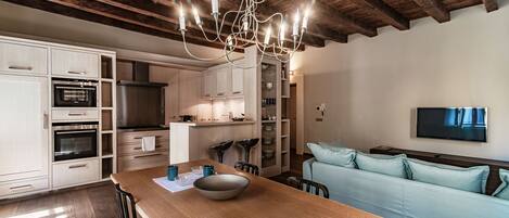 A modern kitchen with white cabinets, a wooden dining table, and a chandelier.