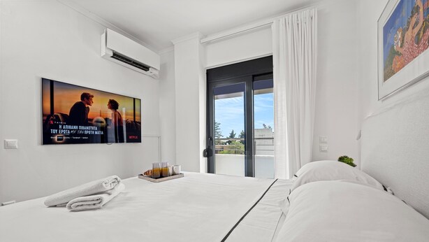 A hotel room with a large bed, a flat-screen TV mounted on the wall, a small table with a tray of drinks, and a window with curtains. - Casa Di Natalia (C6QG+8CQ Rhodes, Greece)