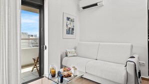 A modern living room with a white sofa, a glass coffee table with breakfast items, and a view through a sliding door to an outdoor balcony. - Casa Di Natalia (C6QG+8CQ Rhodes, Greece)