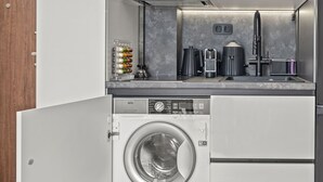 A compact kitchen with a built-in washer and dryer, a coffee maker, and a kettle. - Casa Di Natalia (C6QG+8CQ Rhodes, Greece)