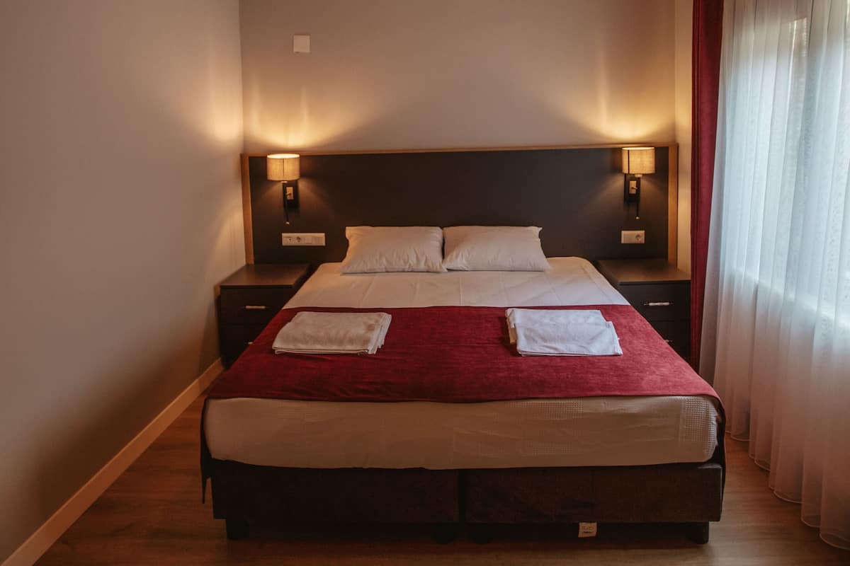 A bedroom with a wooden ceiling, a bed with white linens, two bedside lamps, and a red throw blanket.