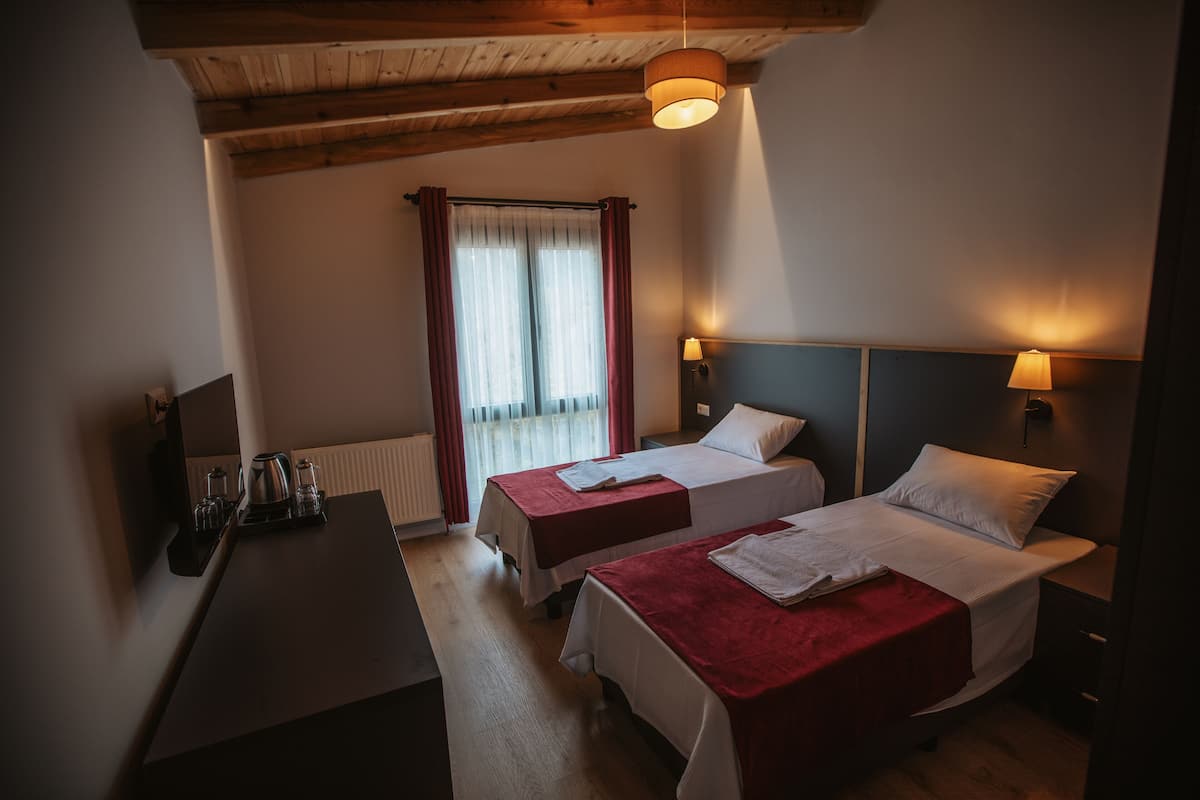A hotel room with two beds, a desk, and a window with curtains.