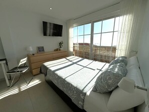 A bedroom with a bed, a dresser, a chair, a TV, and a window with a view.